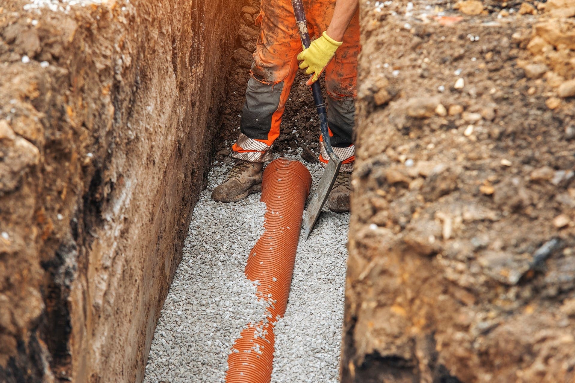 Worker installing drainage pipe in trench.
