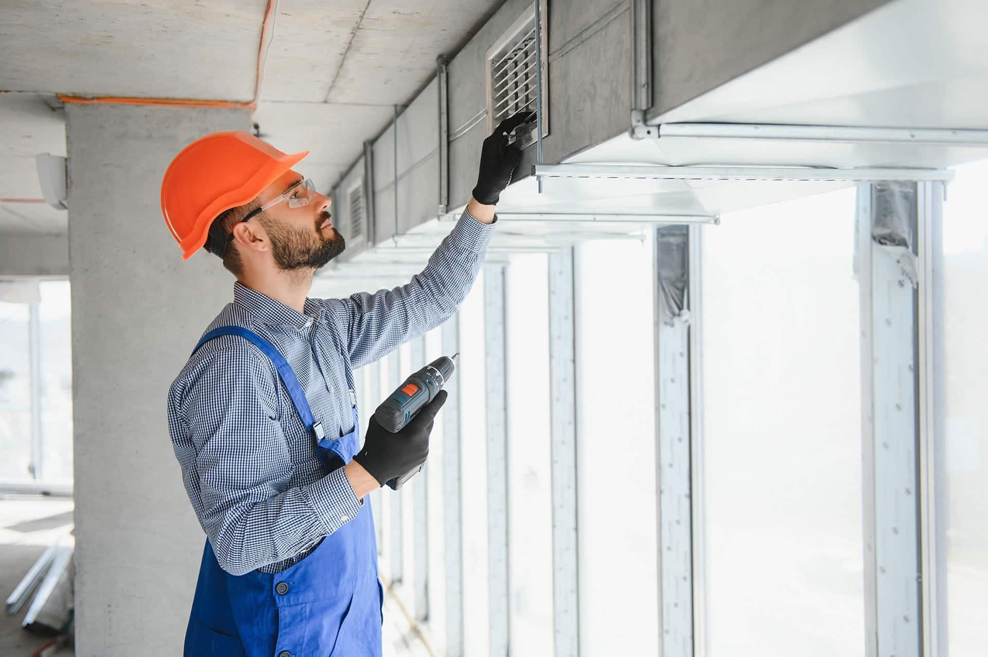 Construction worker inspecting air duct with drill.