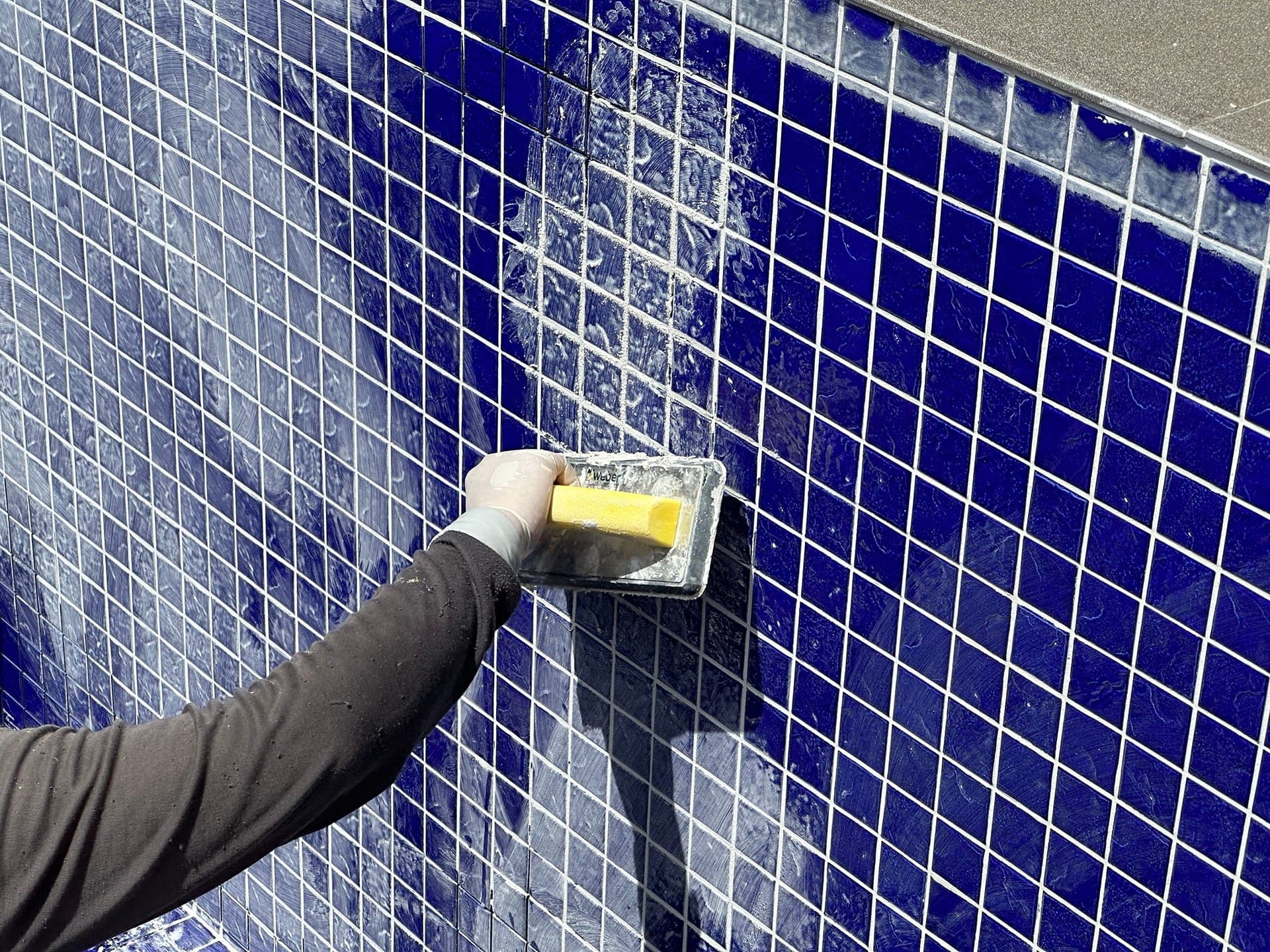 Applying grout to blue tiled wall