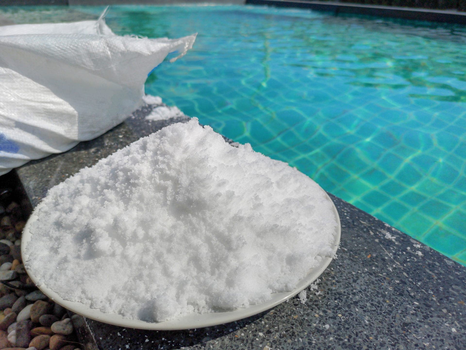 Bowl of pool salt beside swimming pool edge.