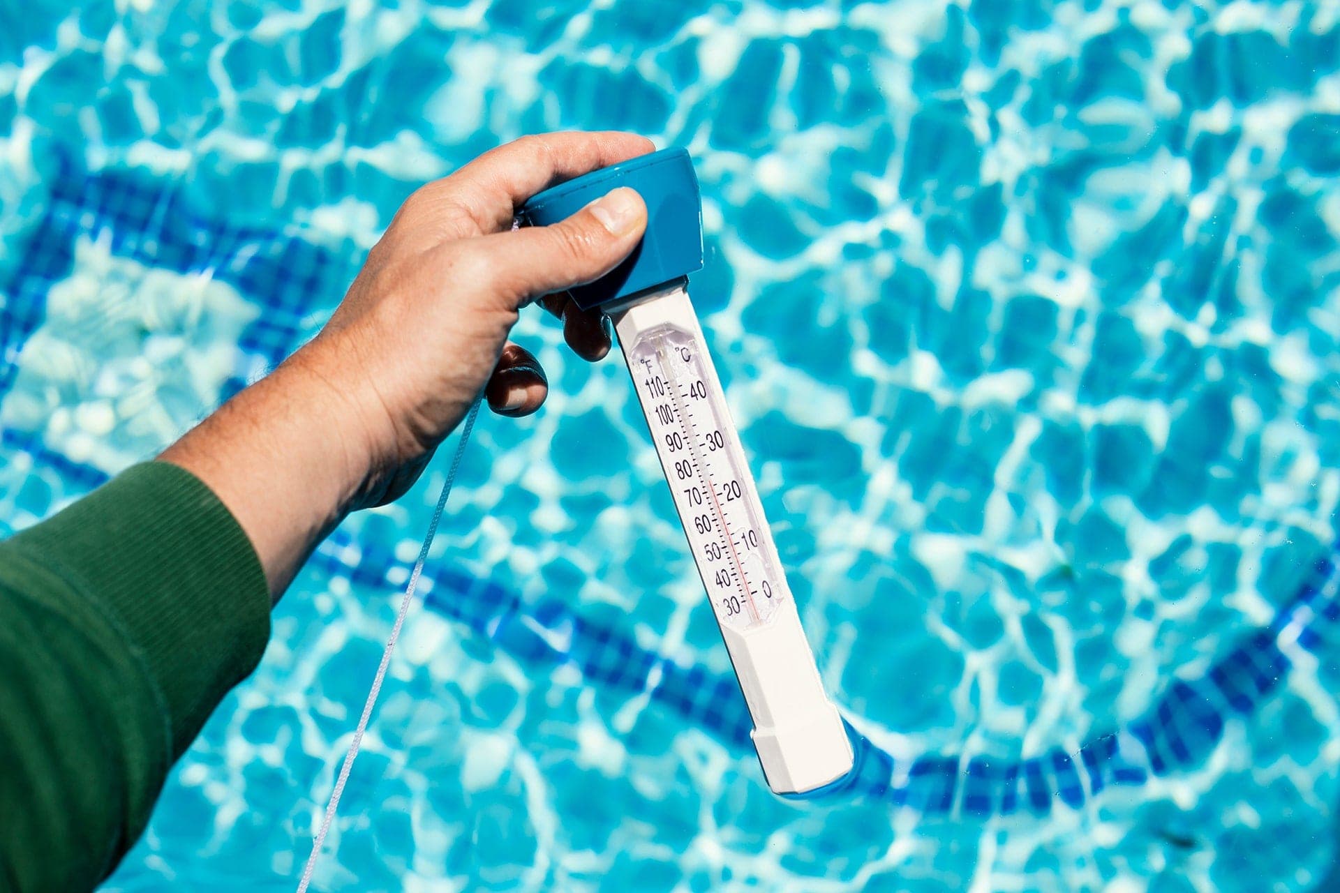 Hand holding pool thermometer over water