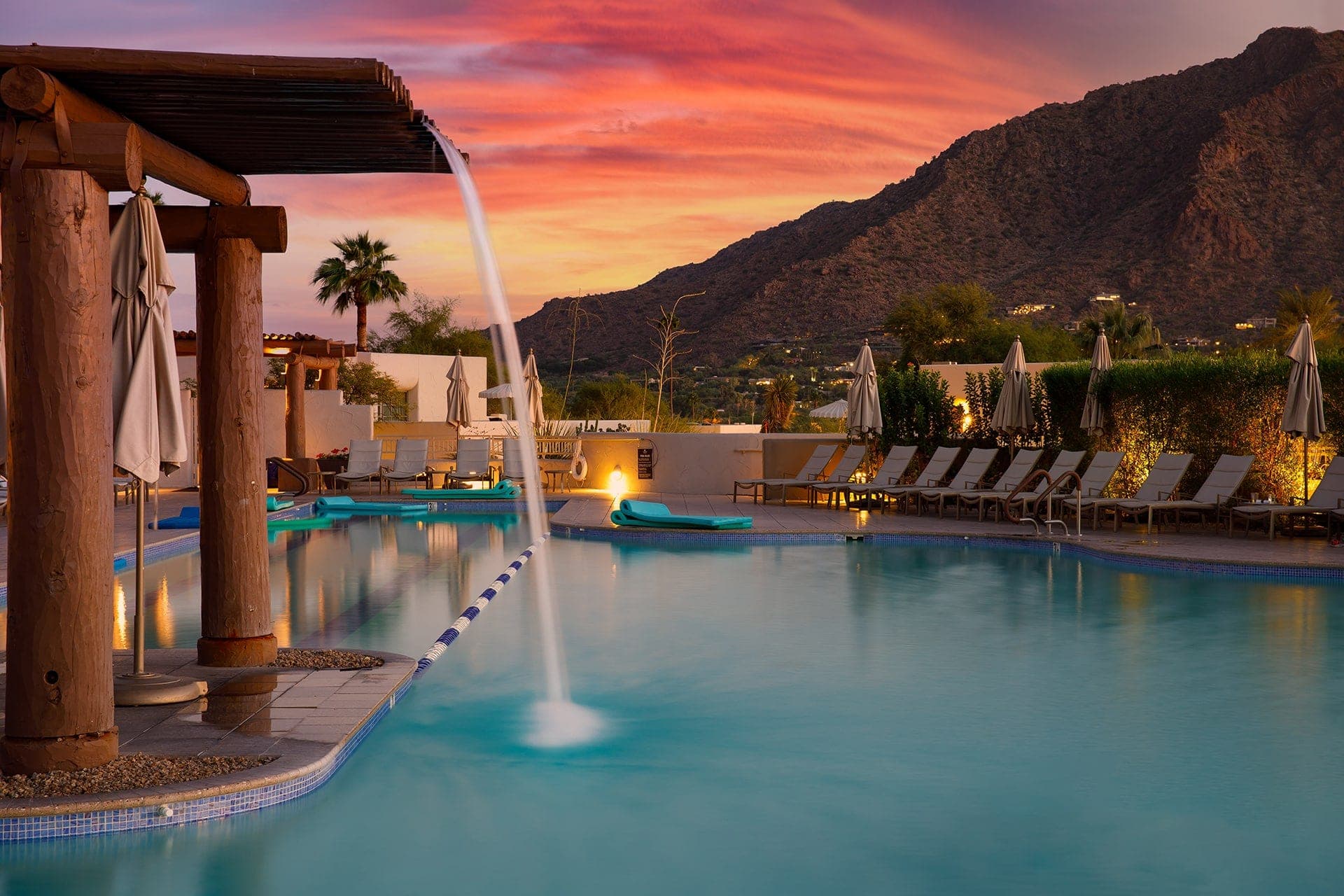 Luxury resort pool at sunset with mountain view.
